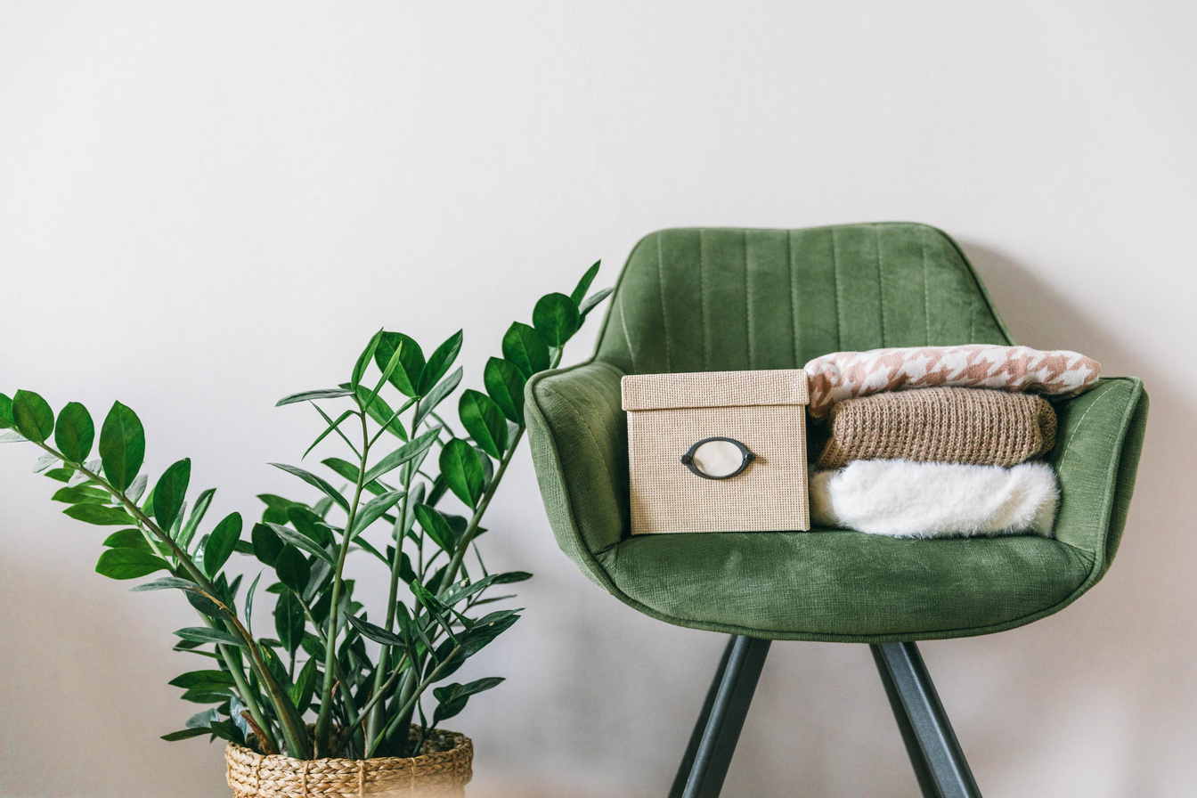 Stack of clothes on a green chair in a light room. Home space organization, spring cleaning and decluttering